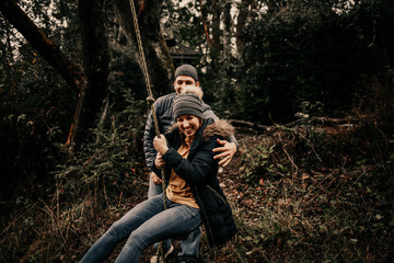 Happy couple swinging on forest rope swing