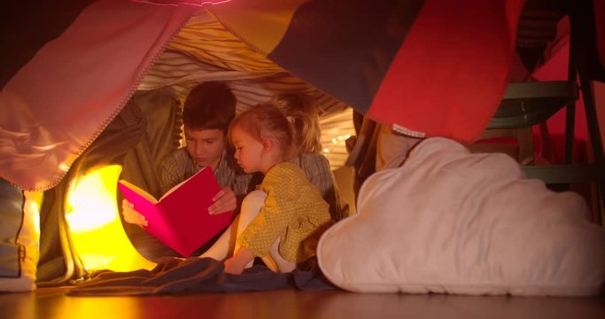 Young children reading a night story in their blanket fort