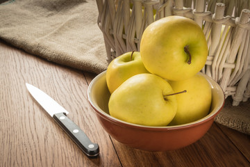 a wooden basket of white color with apples. stands on the table. next to a brown bowl are oranges