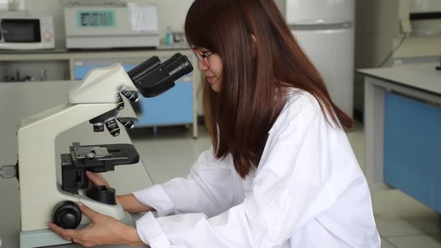 Asian Thai university college girl student or female scientist showing happy expression before looking through microscope for microscopic study in laboratory. 