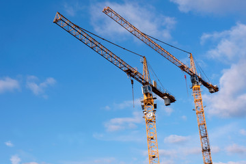 Two yellow construction cranes against blue sky with a few clouds - development in the city- copy space, design element