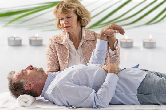 Hypnotherapist holding her patients wrist in therapists officewith warm candle abd greenery in background