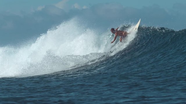 SLOW MOTION: Surfer riding a big ocean wave does a sharp turn and sprays water everywhere. Athletic man on active vacation in sunny Fiji rides his awesome surfboard on picturesque summer afternoon.