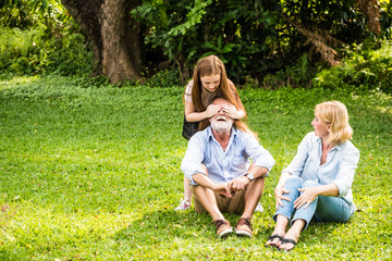 Fototapeta premium Happy family having fun together in the garden. Father, mother and daughter sitting on grass in a park.