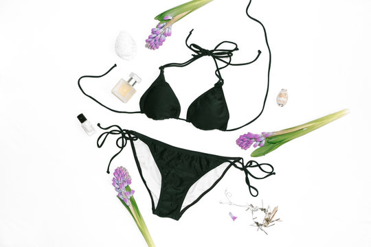 Swimsuit with feminine accessories and lilac flowers on white background. Flatlay, top view. Summer concept
