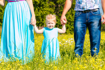 Fototapeta premium Young happy caucasian family with baby girl look at camera. celebration fathers day outdoors. hafving fun. Summer, green flowers field