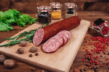 Dried sausage on a wooden board with rosemary and spices. A piece of sausage is pinned on the fork....