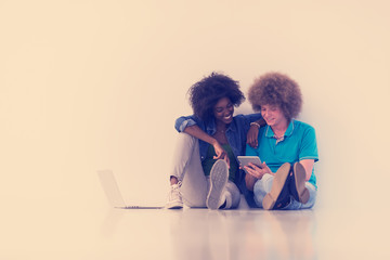 multiethnic couple sitting on the floor with a laptop and tablet
