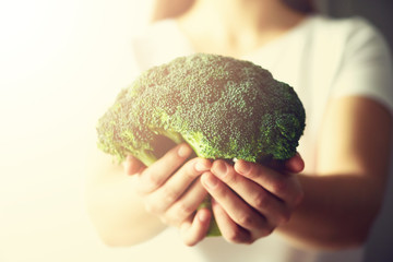 Woman in white T-shirt holding broccoli in hands. Copy space. Healthy clean detox eating concept. Vegetarian, vegan, raw concept. Toned effect with sunlight