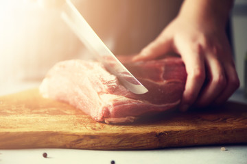 Wooman hands cutting beef meat on wooden chopping board, rosemary, oil, salt, pepper. Girk cooking pork meat on white kitchen backgound. Copy space. Sunlight, toned effect
