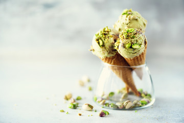 Green ice cream in waffle cone with chocolate and pistachio nuts on grey stone background. Summer...