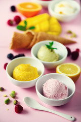 Ice cream balls in bowls, waffle cones, berries, orange, mango, lemon, mint, pistachio on pink shabby chic background. Colorful collection, summer concept