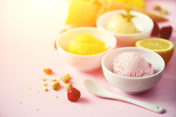 Ice cream balls in bowls, waffle cones, berries, orange, mango, lemon, mint, pistachio on pink shabby chic background. Colorful collection, summer concept