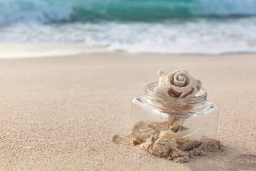 Fototapeta na wymiar Sea Shell In A Glass Jar On The Beach With Sand And Ocean As A Background