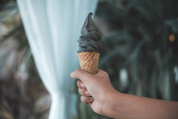 A hand holding charcoal ice cream cone with blur background