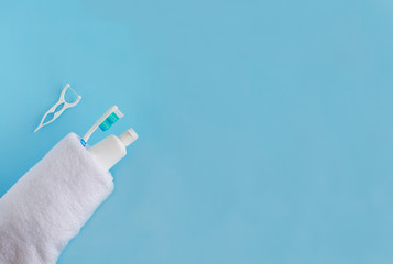 Toothbrushes and toothpaste wrapped in white towel near floss on blue background. Dental and...