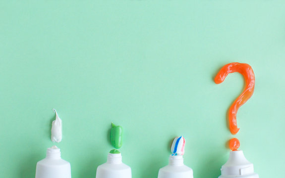 Toothpaste lies on a green background and a question mark. Choice of toothpaste. The concept of dentistry and health. Free space for copying.