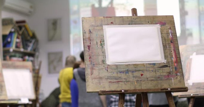 Clear sheet of paper on easel in drawing class against the background of students in the classroom