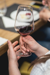 woman holds glass of red wine. people consider the color of the wine and try how it smells in different glasses