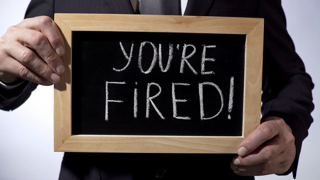 Youre fired with exclamation written on blackboard, businessman holding sign