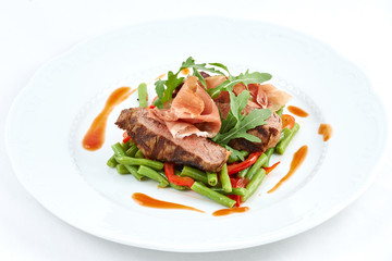 Grilled beef with pork slices and boiled pepper, green beans, fresh arugula and sauce on a white plate.