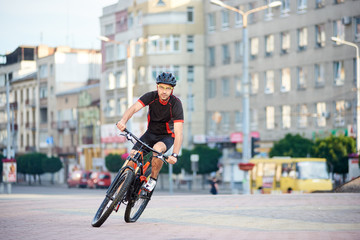 Guy bicyclist posing in cycling clothes and helmet on bike for sport campaign in front of city building. Sportsman exercising outdoors, rest after working day. Concept of healthy lifestyle