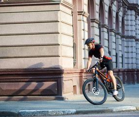 Fototapeta premium Sportsman in professional cycling sportswear and protective helmet riding bicycle along old historical city streets, taking turns. Cyclist exploring town by bike. Concept of healthy lifestyle