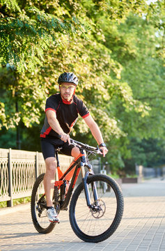Male biker in cycling sportswear and protective helmet riding on bike near green park. Concept of healthy lifestyle, sport advertising, outdoor activities
