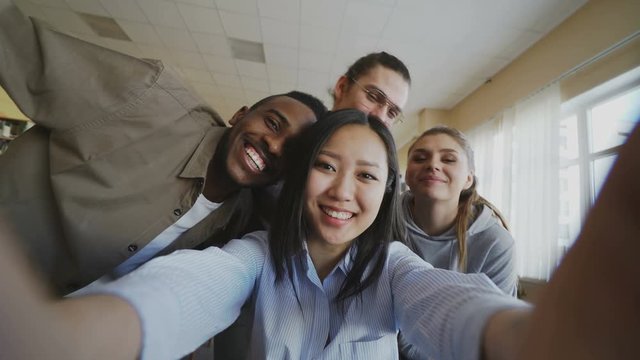 Point of view of asian girl holding smartphone taking selfie photos with cheerful classmates and have fun at university library