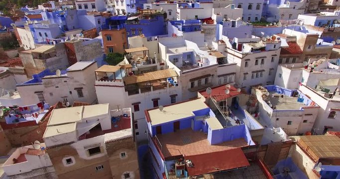 Low aerial view over the rooftops of Chefchaouen in Morocco. Laundry dries on flat terraces between blue painted walls in a charming honest scene of daily life in the dense old blue medina.
