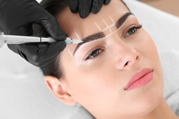 Naklejka premium Młoda kobieta przechodzi procedurę makijażu permanentnego brwi w salonie piękności