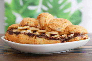 Tasty croissant with banana and chocolate sauce on plate, closeup