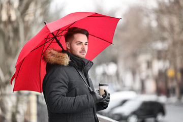 Young man in warm clothes with red umbrella outdoors