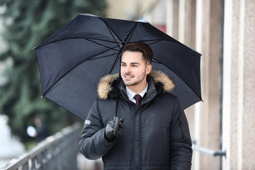 Young man in warm clothes with dark umbrella outdoors