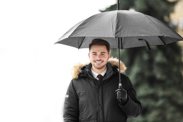 Young man in warm clothes with dark umbrella outdoors