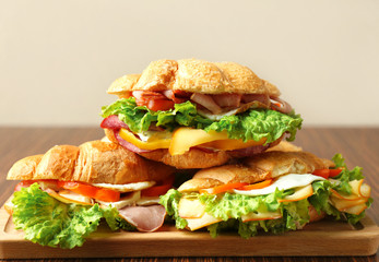 Tasty croissant sandwiches on wooden board, closeup