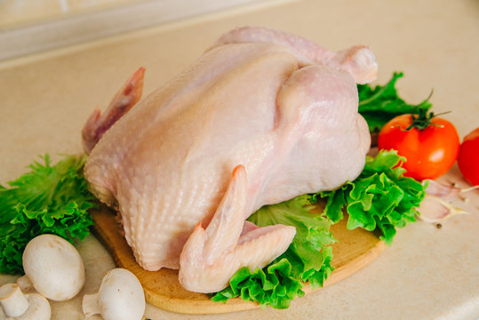 raw chicken on the cutting board, with tomatoes, garlic, mushrooms and seasonings on lettuce leaves, on the table top, for grilling or for a picnic