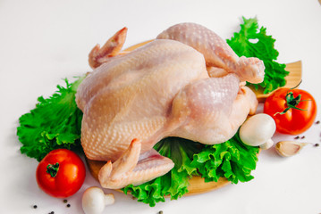 raw chicken on the cutting board, with tomatoes, garlic, mushrooms and seasonings on lettuce leaves, isolated on white background