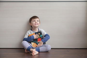 Naklejka premium A beautiful child is sitting on the floor, hugging a book and dreaming about space.