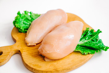 Raw chicken fillets on wooden cutting board with lettuce leaves, on white background