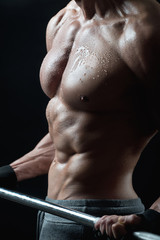 Obraz premium Male sporty wet glossy body with tight muscles and a barbell in hands on a black isolated background.
