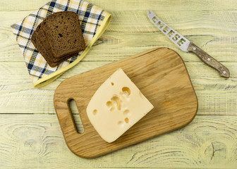 A slice of cheese on a cutting board and black bread next to a wooden surface.