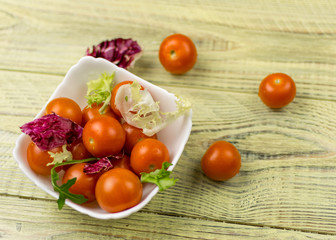 Cherry tomatoes in a white plate on a wooden background.