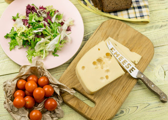 A piece of cheese and fresh vegetables next to a wooden surface. Preparation of a vegetarian salad.