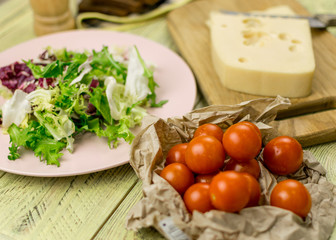 A piece of cheese and fresh vegetables next to a wooden surface.