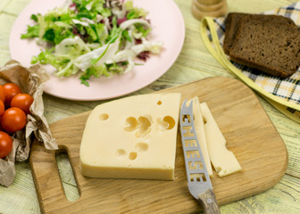A piece of cheese and fresh vegetables next to a wooden surface.