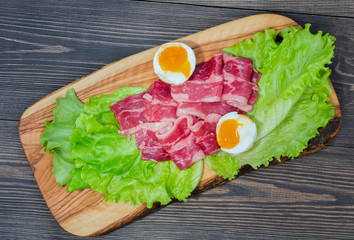 Marbled beef with egg, raw meat on an olive board with lettuce leaves on a dark background of natural wood