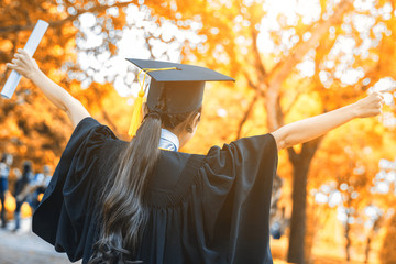 Graduated woman students wearing graduation hat and gown, congratulations with autumn tree background
