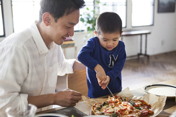 ピザをナイフで切り分ける男の子。パパに見守られながら、楽しい作業。