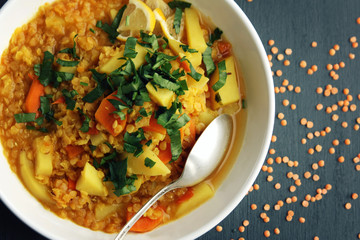 Red lentil stew with potato, carrot and turmeric. Toned photo. Healthy lunch on the round white plate. Colorful vegan dish with potato, carrot and turmeric. European cuisine. Vegetarian. Top view.